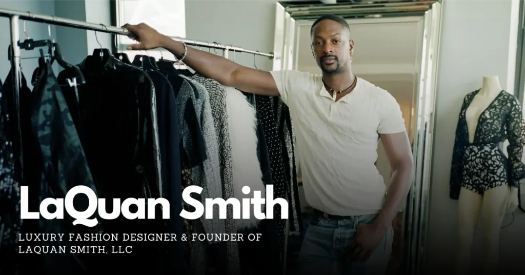 LaQuan Smith Standing with a hand in his pocket and an arm resting on a clothing rack