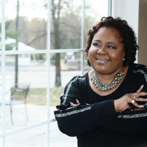 Bulinda standing by a window and smiling with her arms crossed over her chest