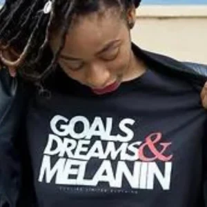 woman with dread locs looking down at her tshirt that says goals,dreams & melanin