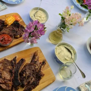 meat on cutting boards, vases of flowers, dish of sauce and a drink
